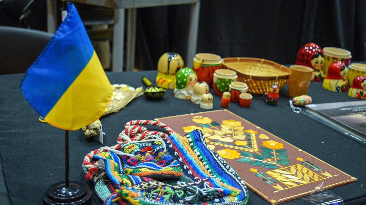 举着乌克兰国旗的看台, 还有一个用刺绣装饰的包, 套娃和一件描绘黄花图案的艺术品.  