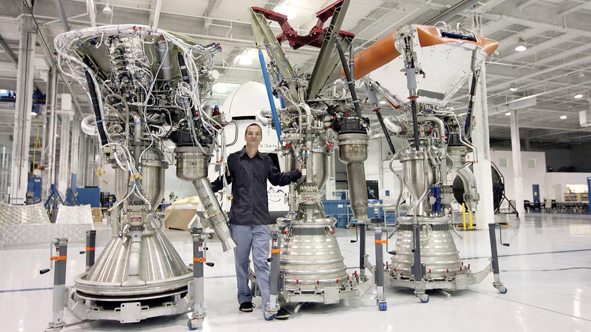 汤姆·穆勒与三个火箭发动机合影，这些发动机几乎是他身高的两倍.
