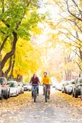Two 学生s ride down Greek Row in the fall, amid changing leaves.